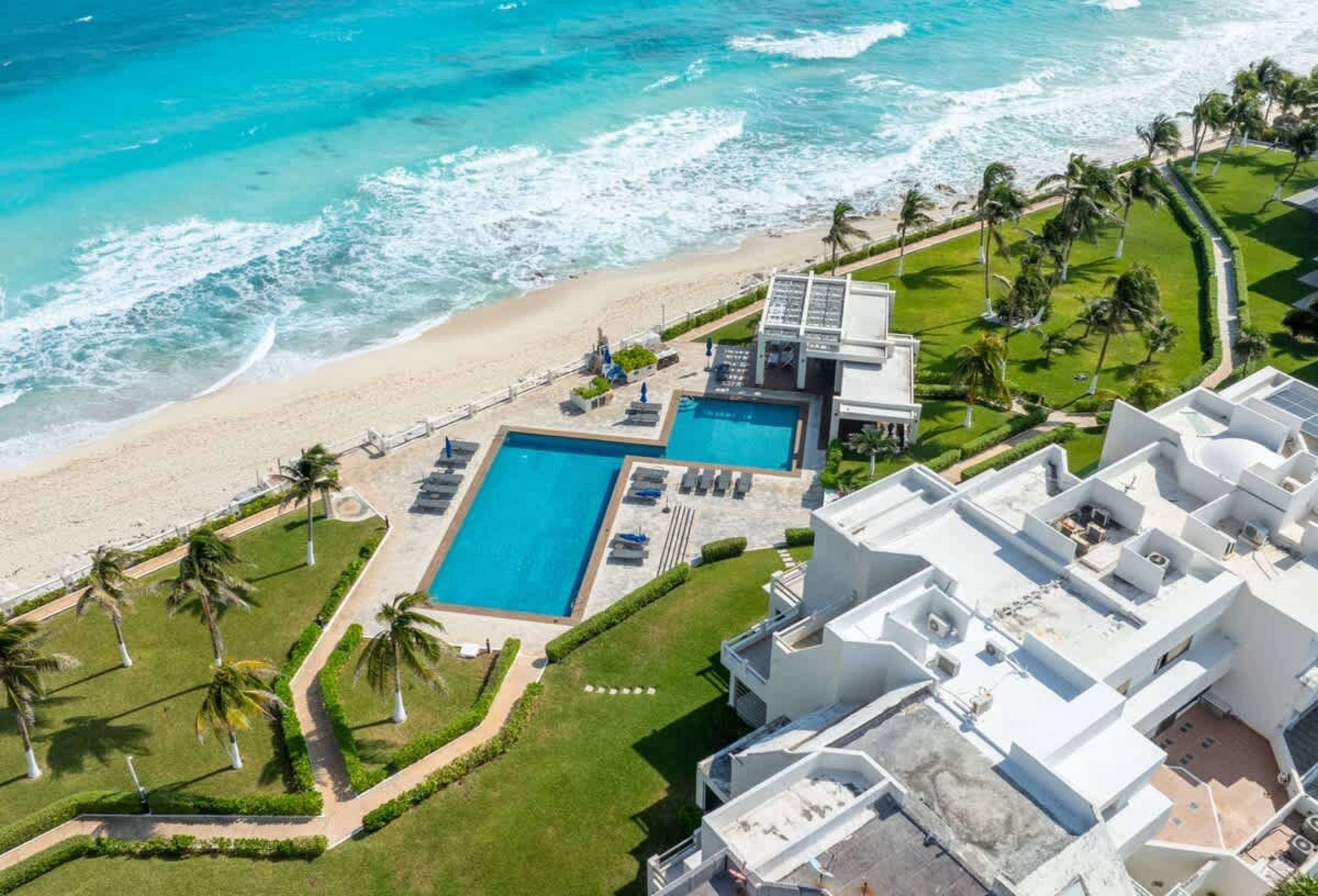 Aerial view of a resort with pools, beach, and palm trees.
