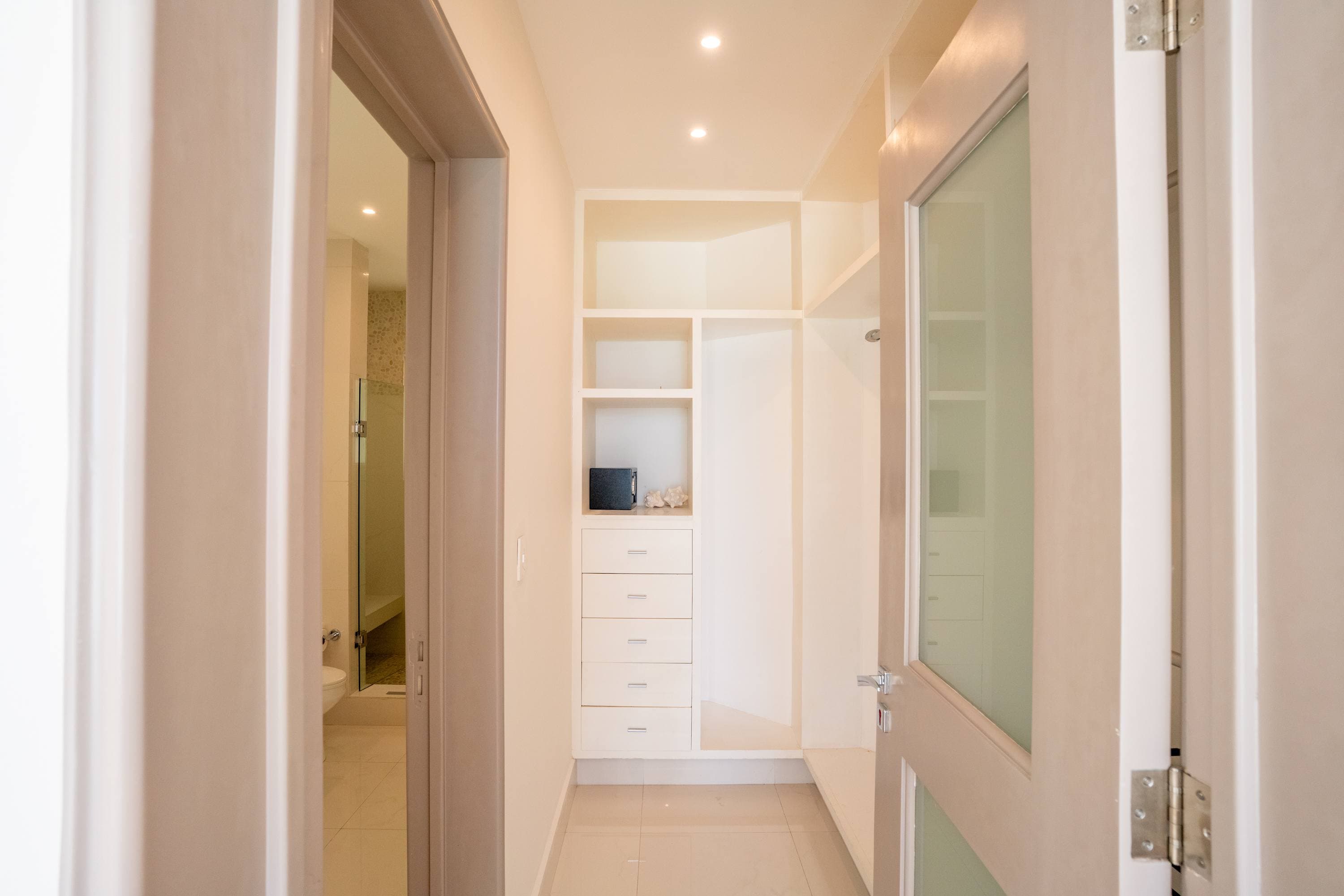An open closet with shelves, drawers, and a safe, next to a bathroom.