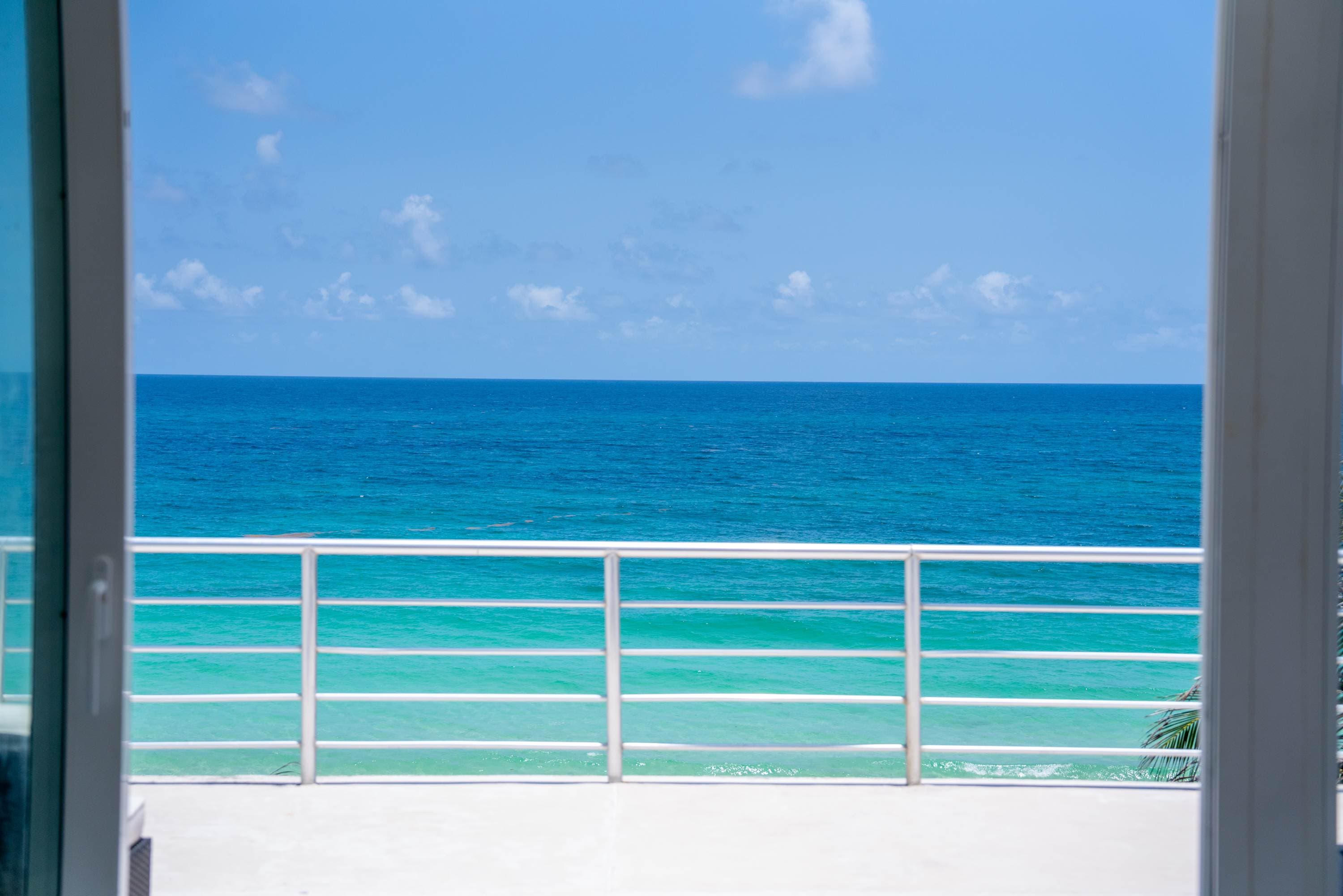 View of the ocean and sky from a balcony through open sliding doors.
