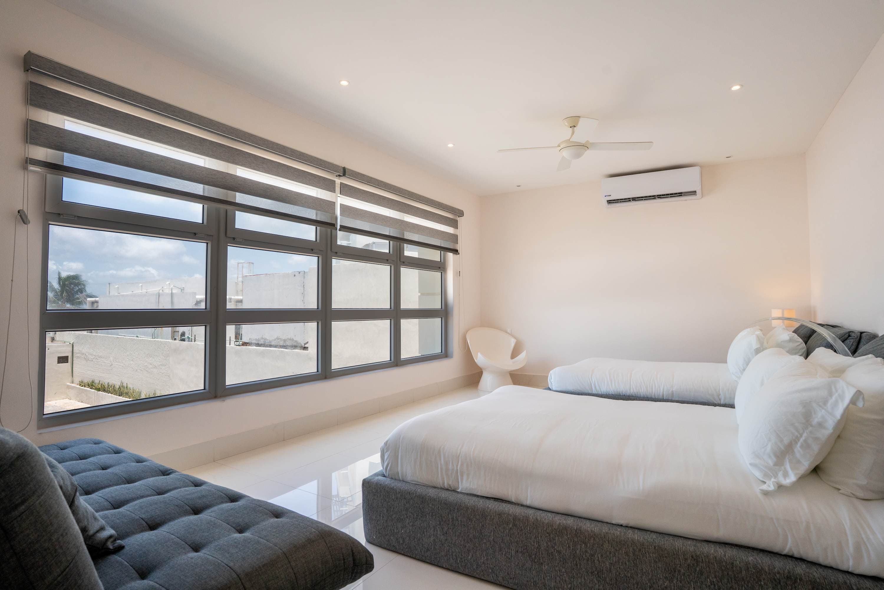 A bedroom with two beds, a sofa, and a large window.
