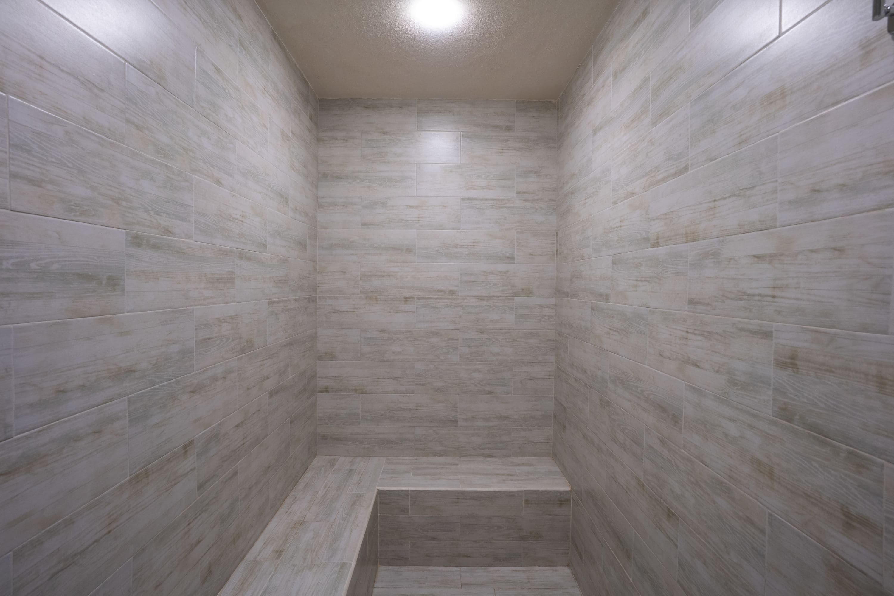 A light-colored, wood-look tiled steam room with a built-in bench.