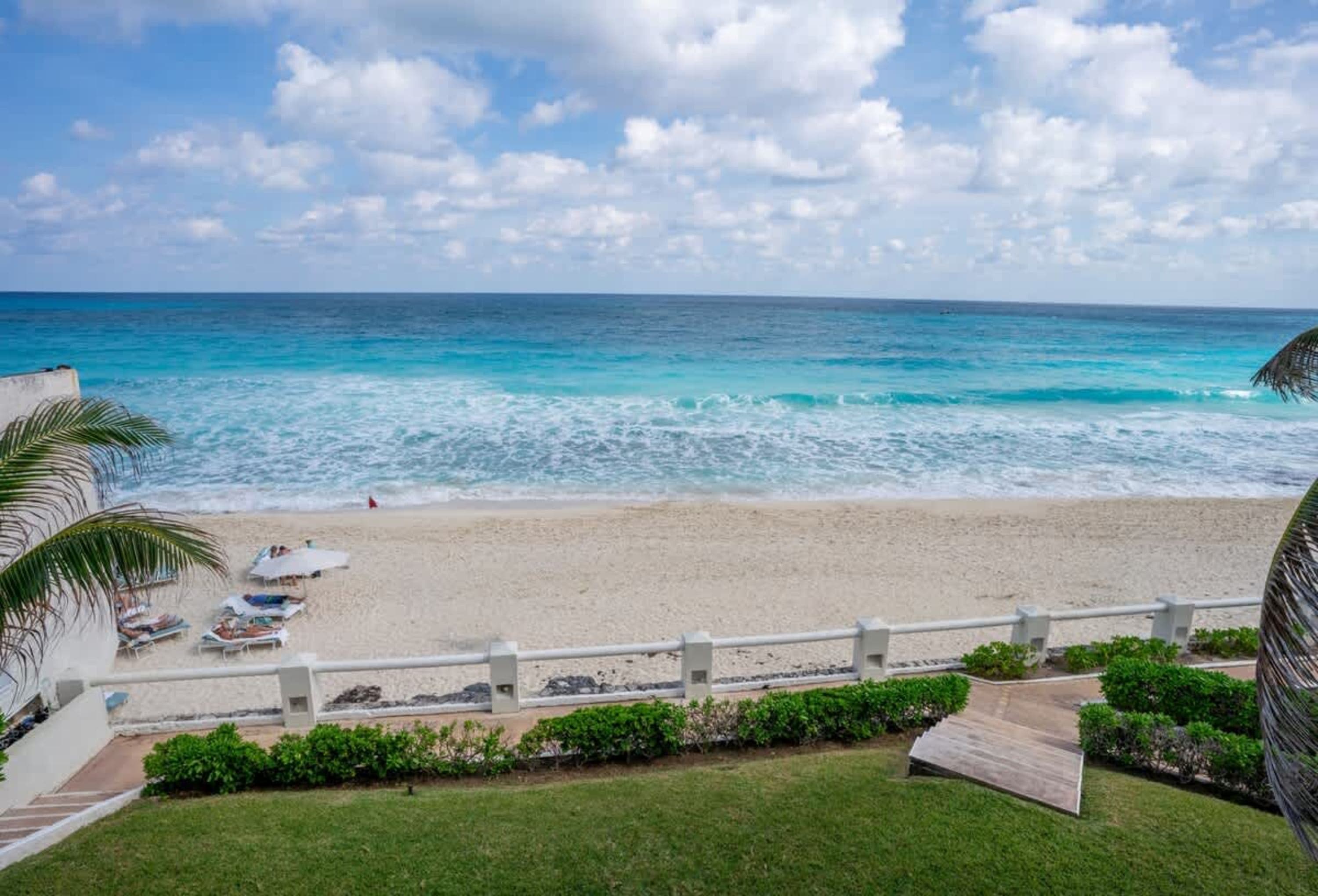 A view of a beautiful beach with turquoise waters, white sand, and lounge chairs.