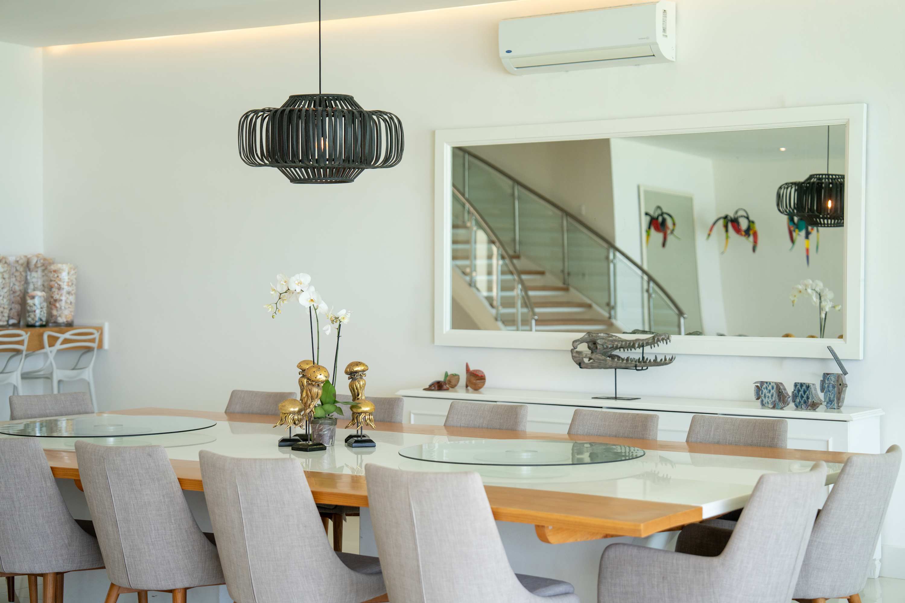 A modern dining room with a large white table, grey chairs, and a black pendant light.