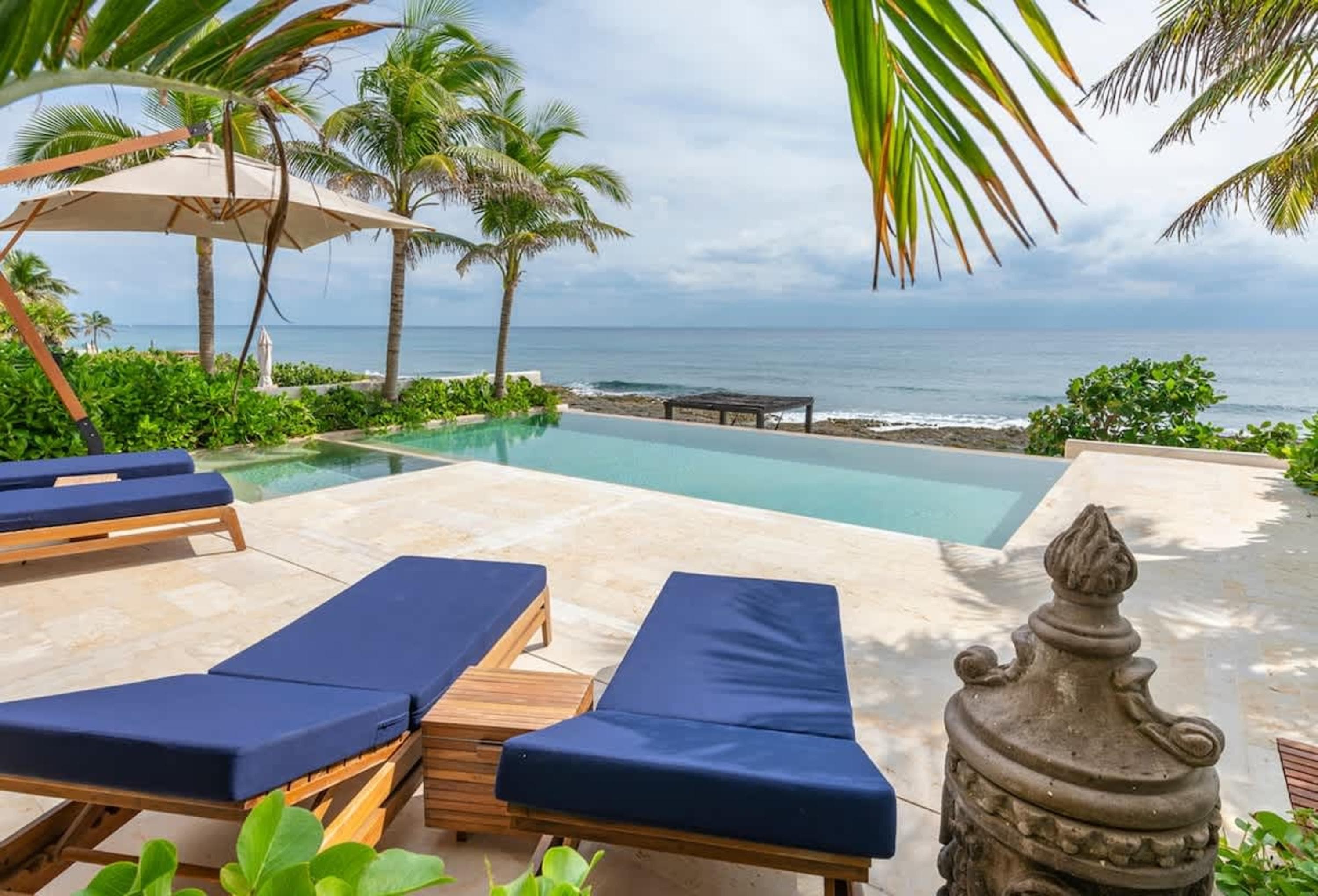 Infinity pool overlooking the ocean with lounge chairs and palm trees.