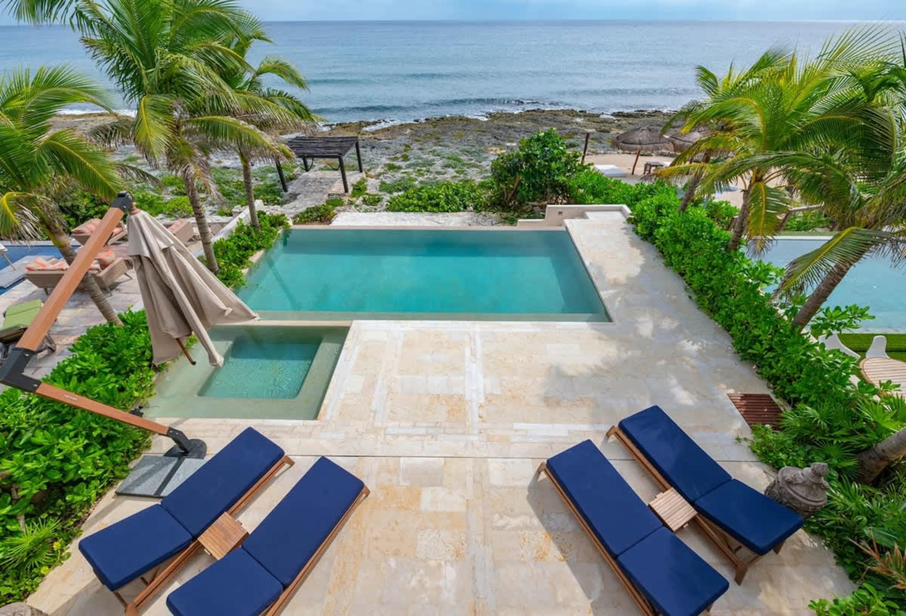 Luxurious oceanfront villa with pool, hot tub, and lounge chairs.