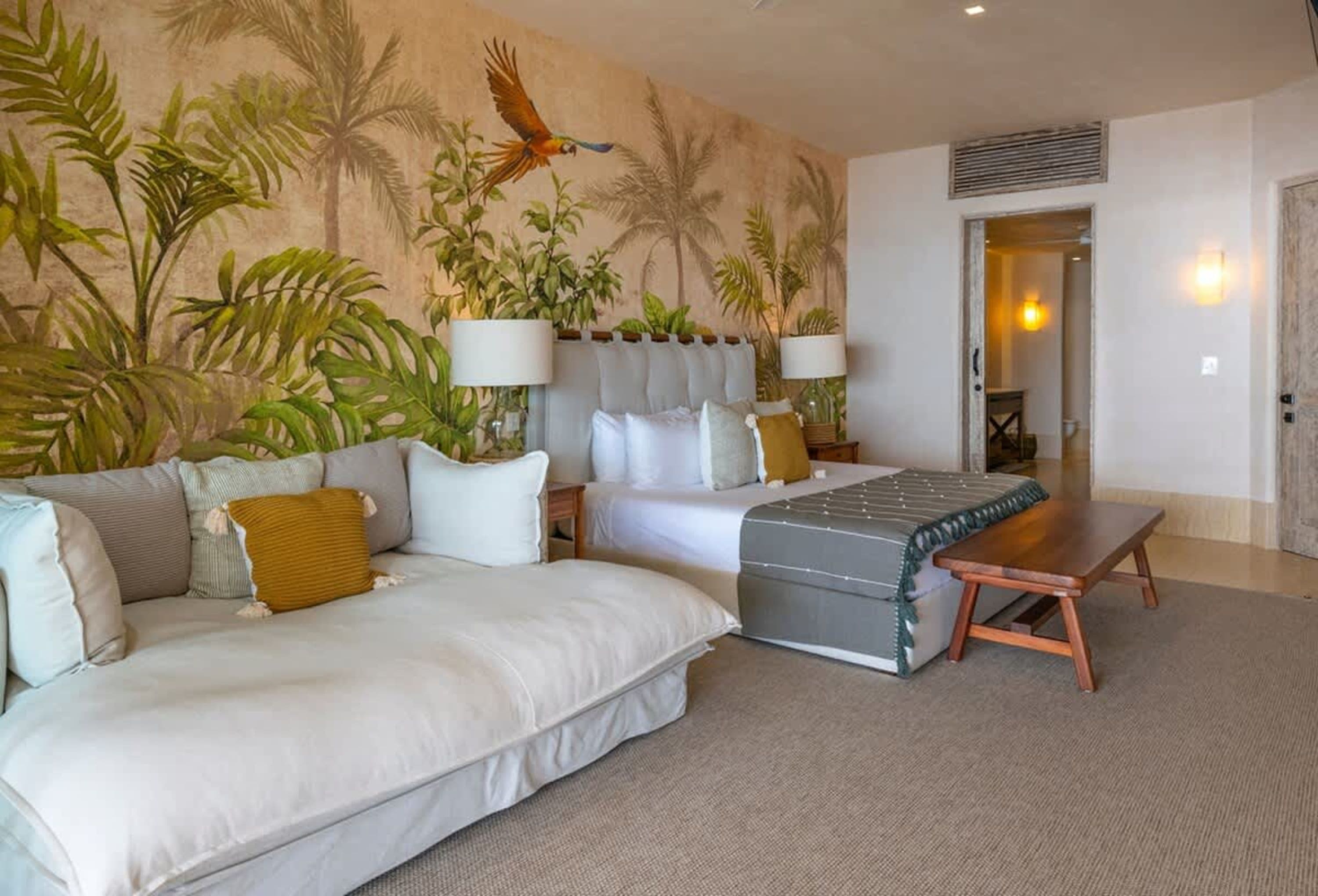 A tropical themed bedroom with a parrot mural, large sofa, and beds.