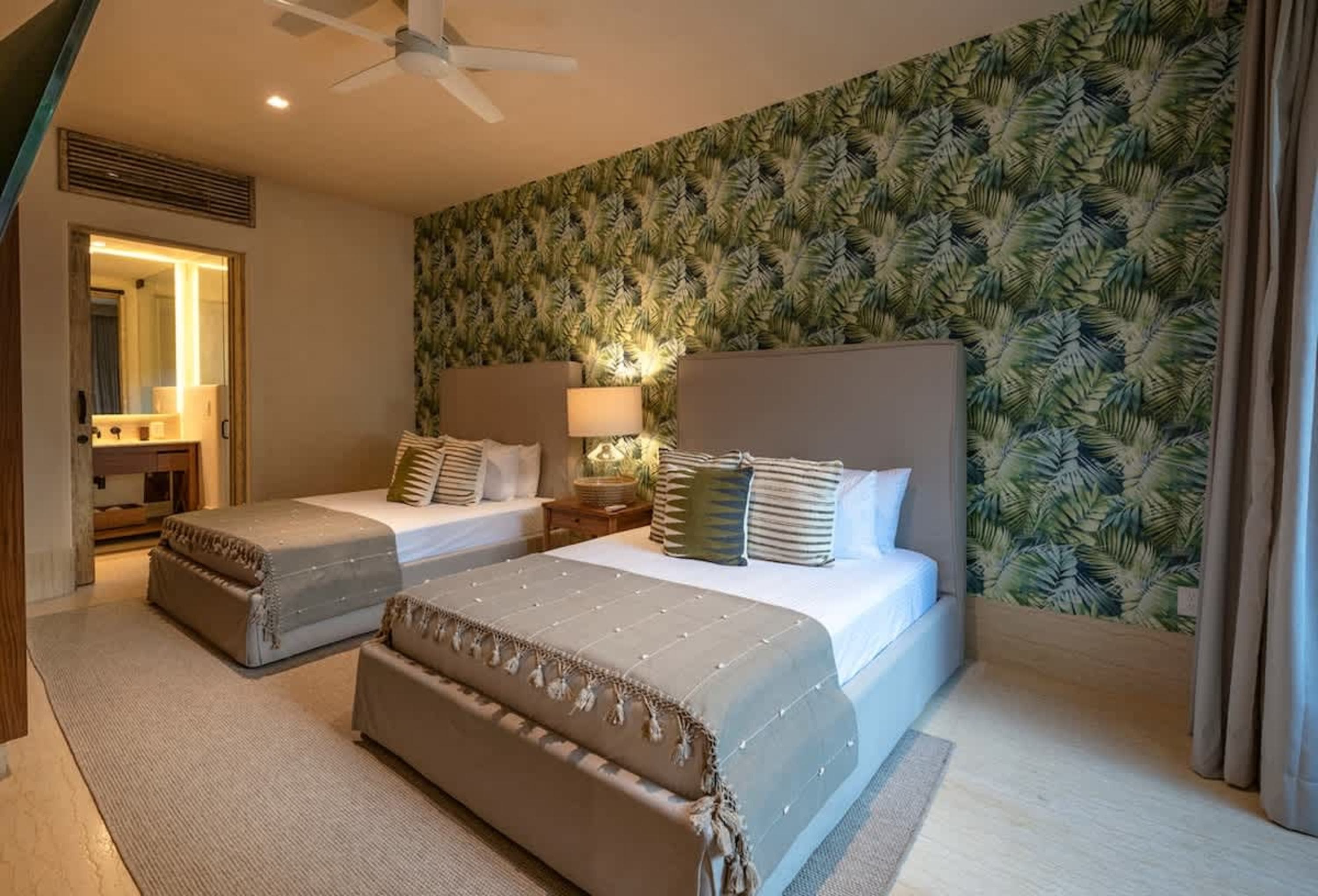 A bedroom with two beds, a tropical-themed wallpaper, and a ceiling fan.