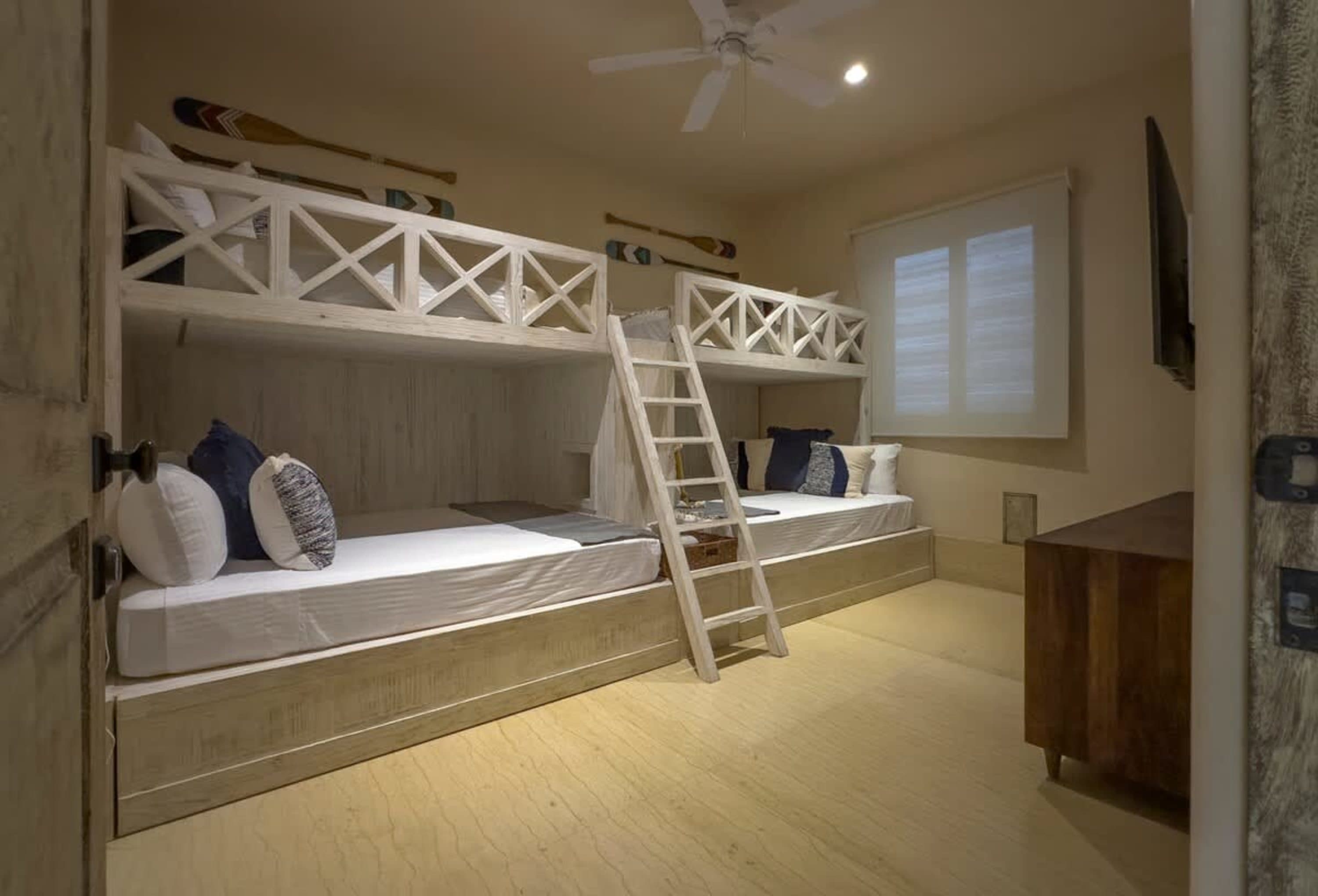 A room with bunk beds, oars on the wall, and a ceiling fan.