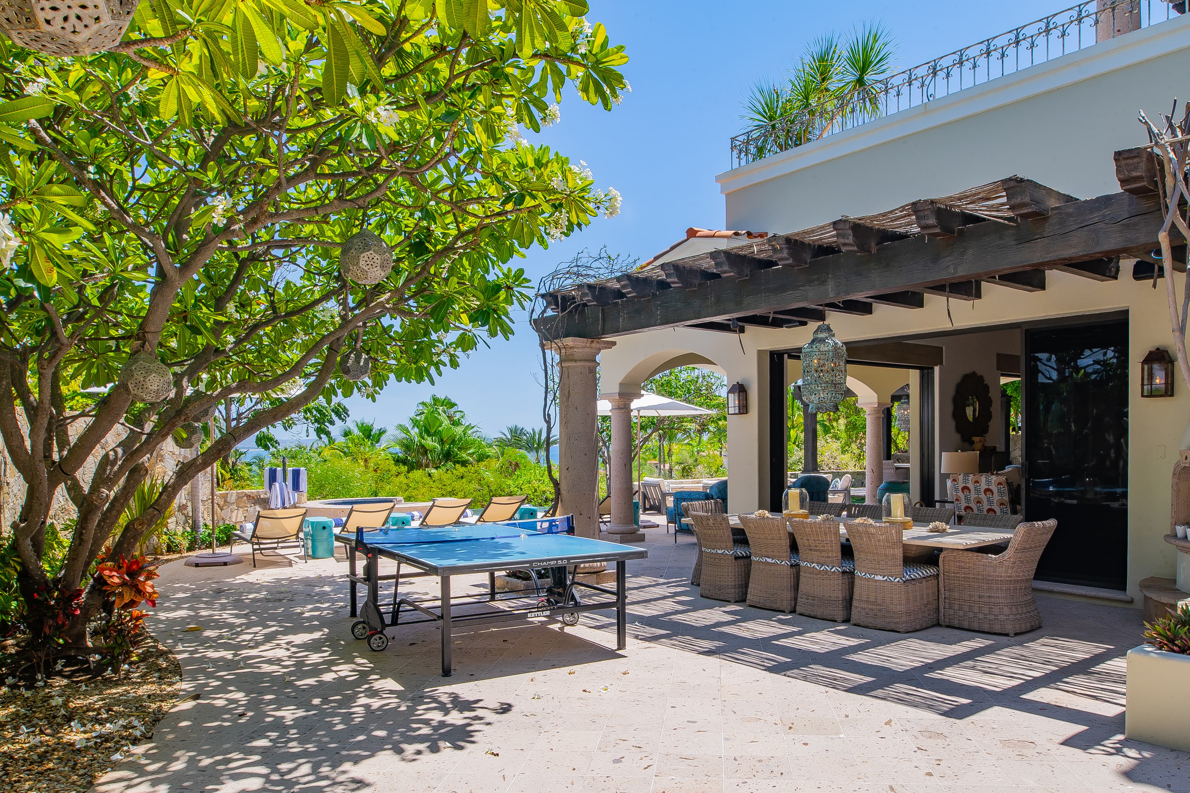 A covered patio overlooking lush tropical grounds offers a shaded spot for alfresco dining or a friendly game of ping pong, blending relaxation with seaside fun.