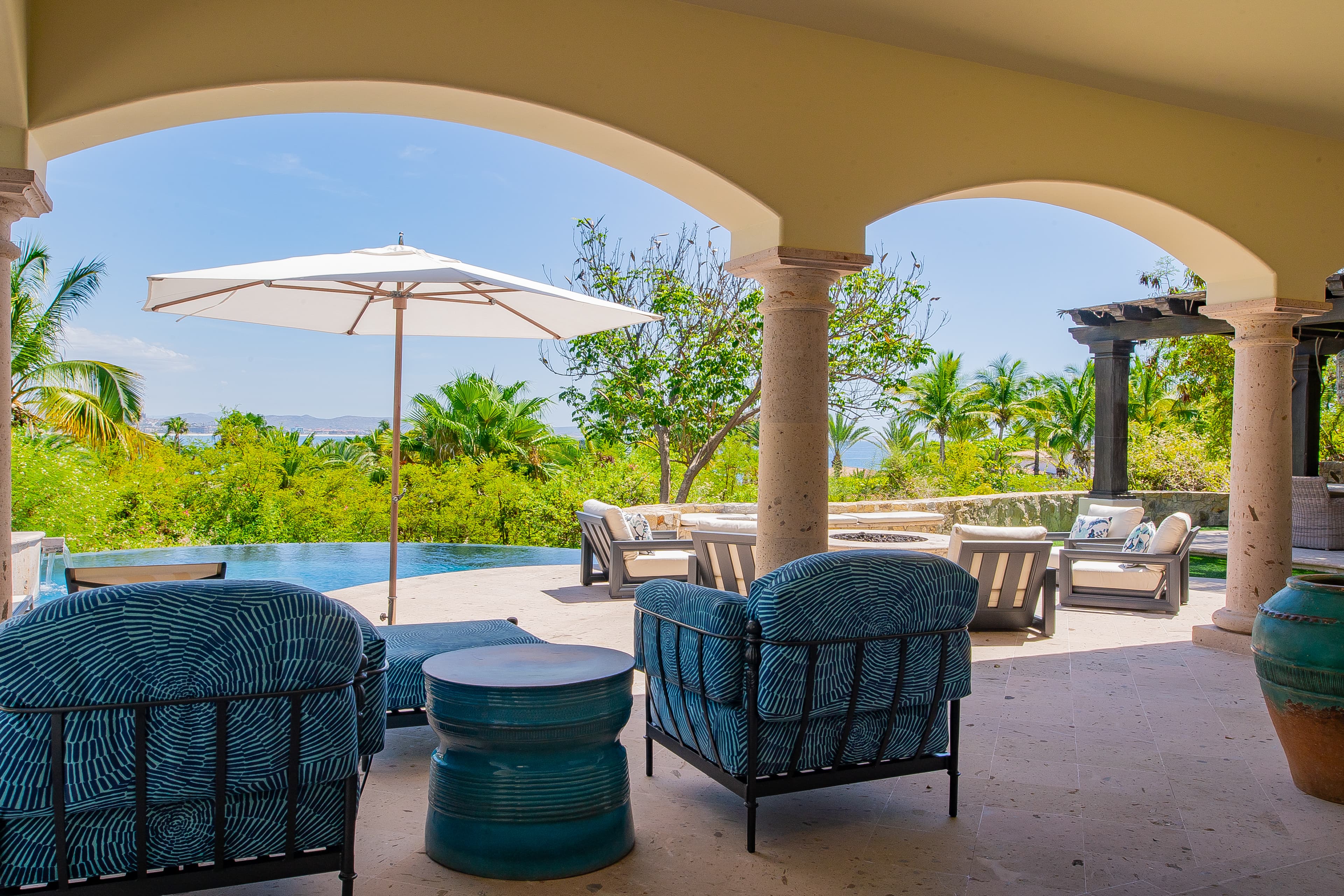 Your private covered terrace offers plush seating and a stunning poolside oasis framed by tropical greenery and sweeping ocean views beyond.