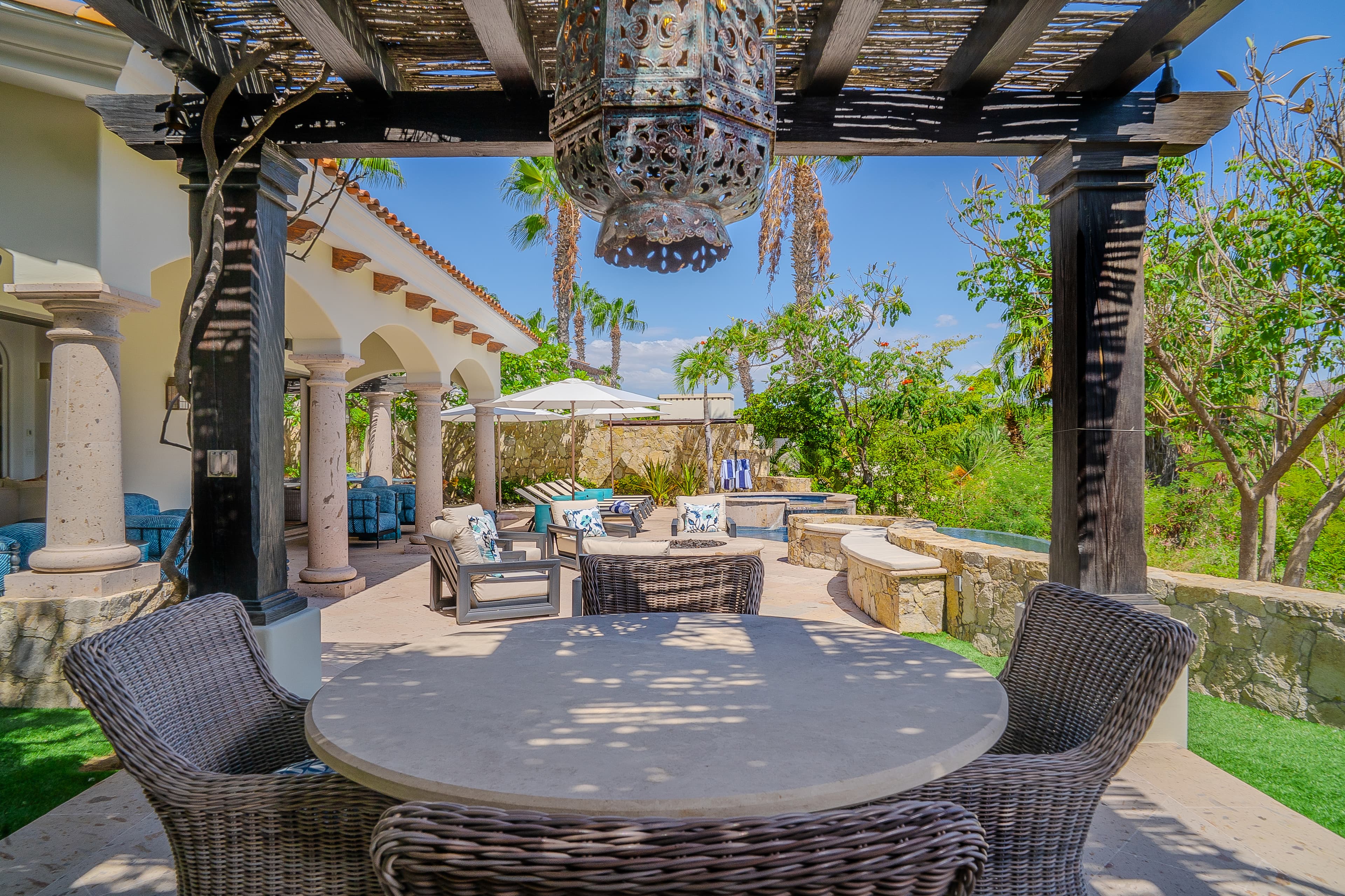 Your private outdoor haven blends elegant stonework with lush greenery, offering shaded seating, poolside loungers, and serene spaces to unwind under hand-carved beams and a decorative lantern.