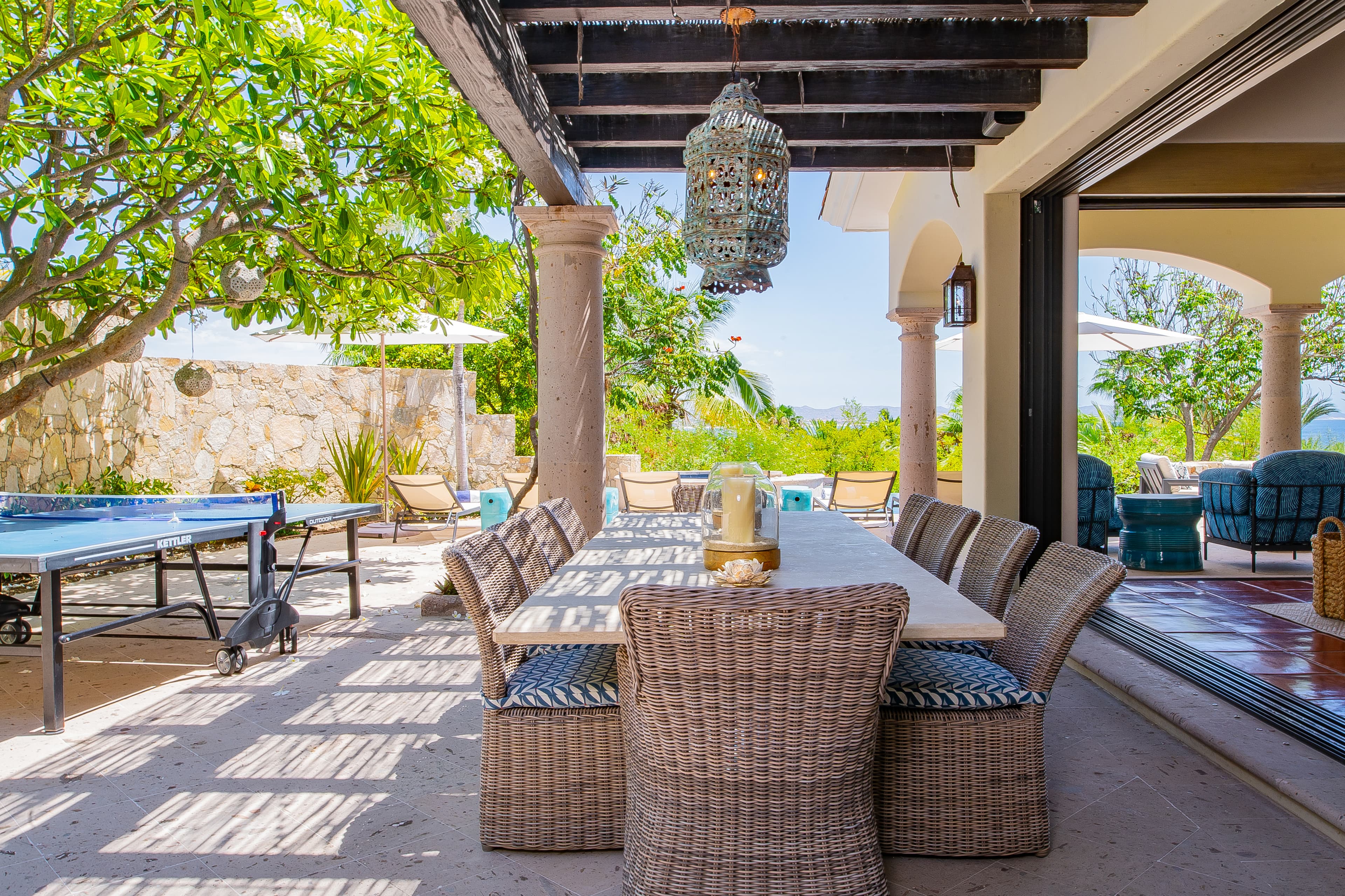 Gather around this beautiful outdoor dining space where dappled sunlight and gentle breezes create your perfect vacation backdrop. Beyond, lounge chairs and a ping-pong table invite leisurely days in paradise.