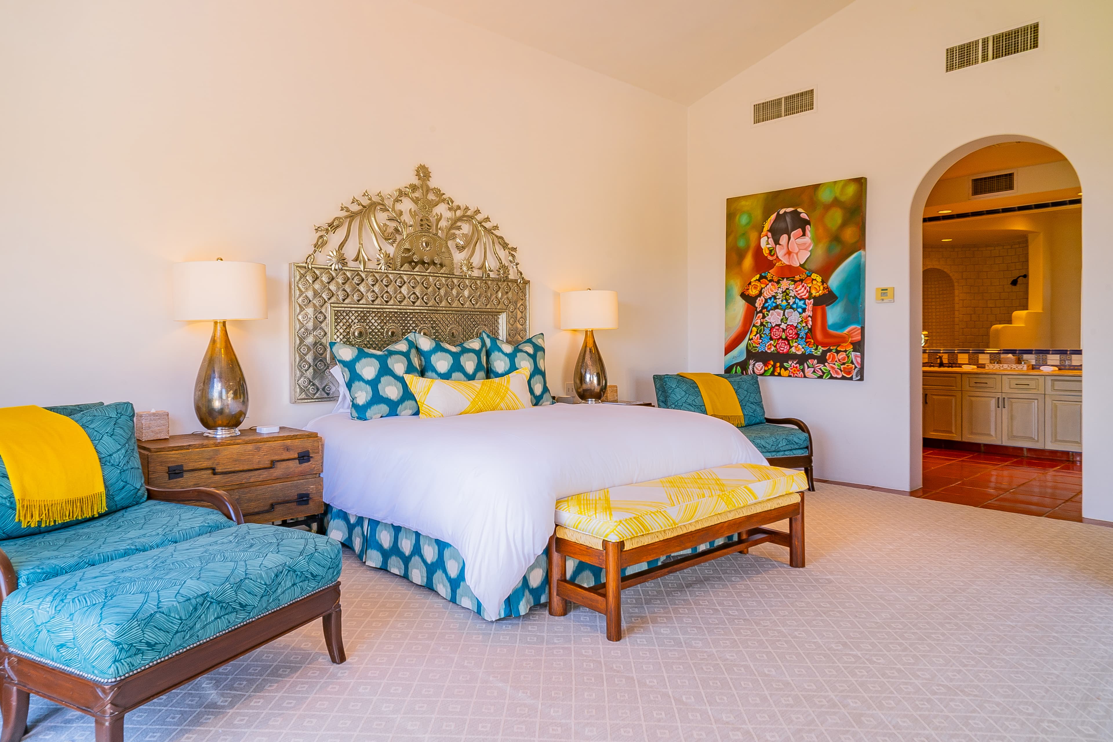 Bedroom 3 · Slip into crisp white linens beneath an ornate headboard, surrounded by cheerful yellow and turquoise accents. Your private ensuite awaits through the elegant arched doorway.