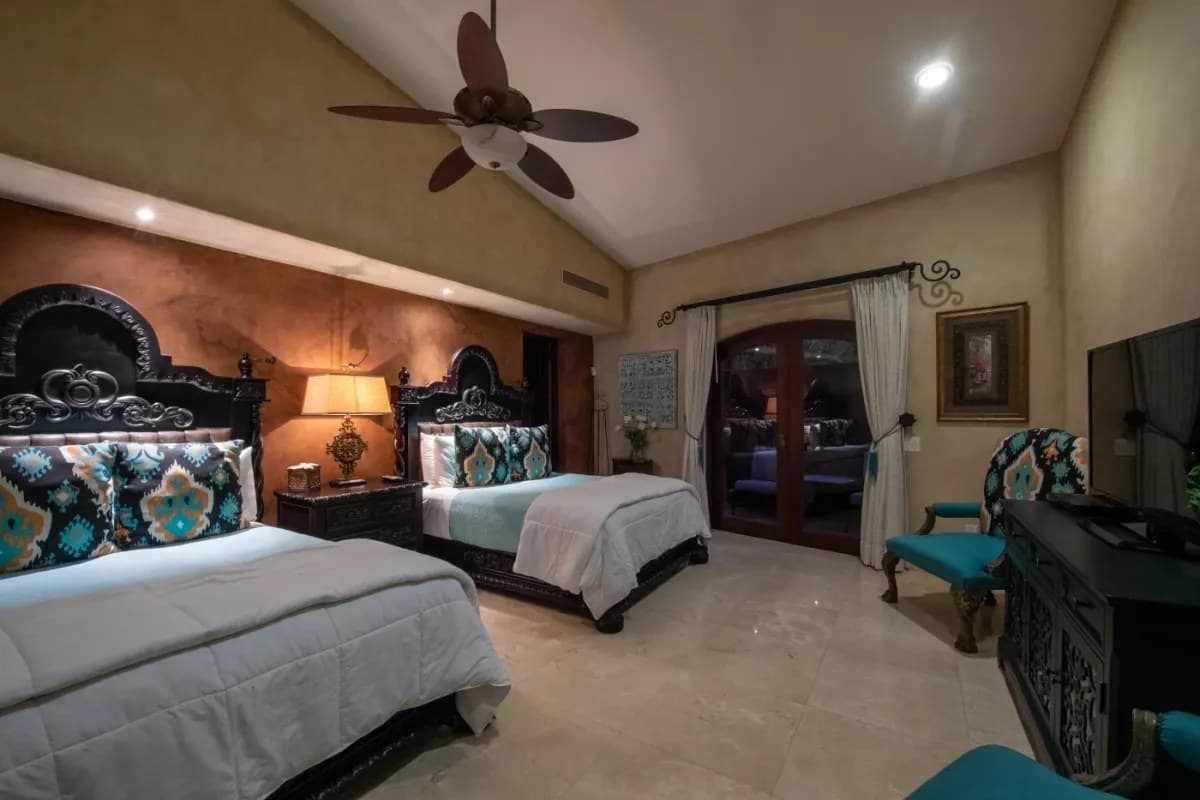 Bedroom 5 · Sink into plush beds with vibrant turquoise accents, relax under the ceiling fan's gentle breeze, and enjoy your favorite shows on the flat-screen TV in this elegant retreat.
