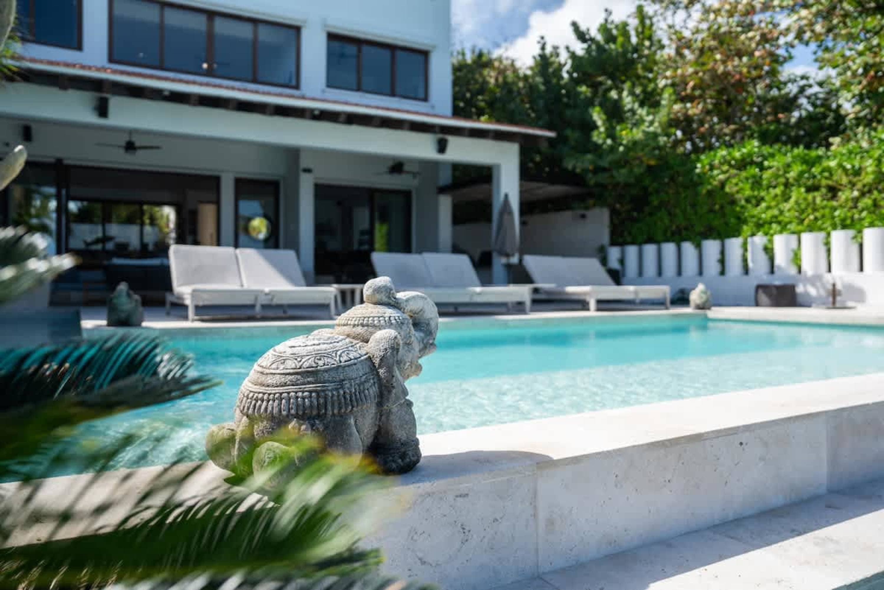 A stone elephant statue sits by a pool in front of a modern house.