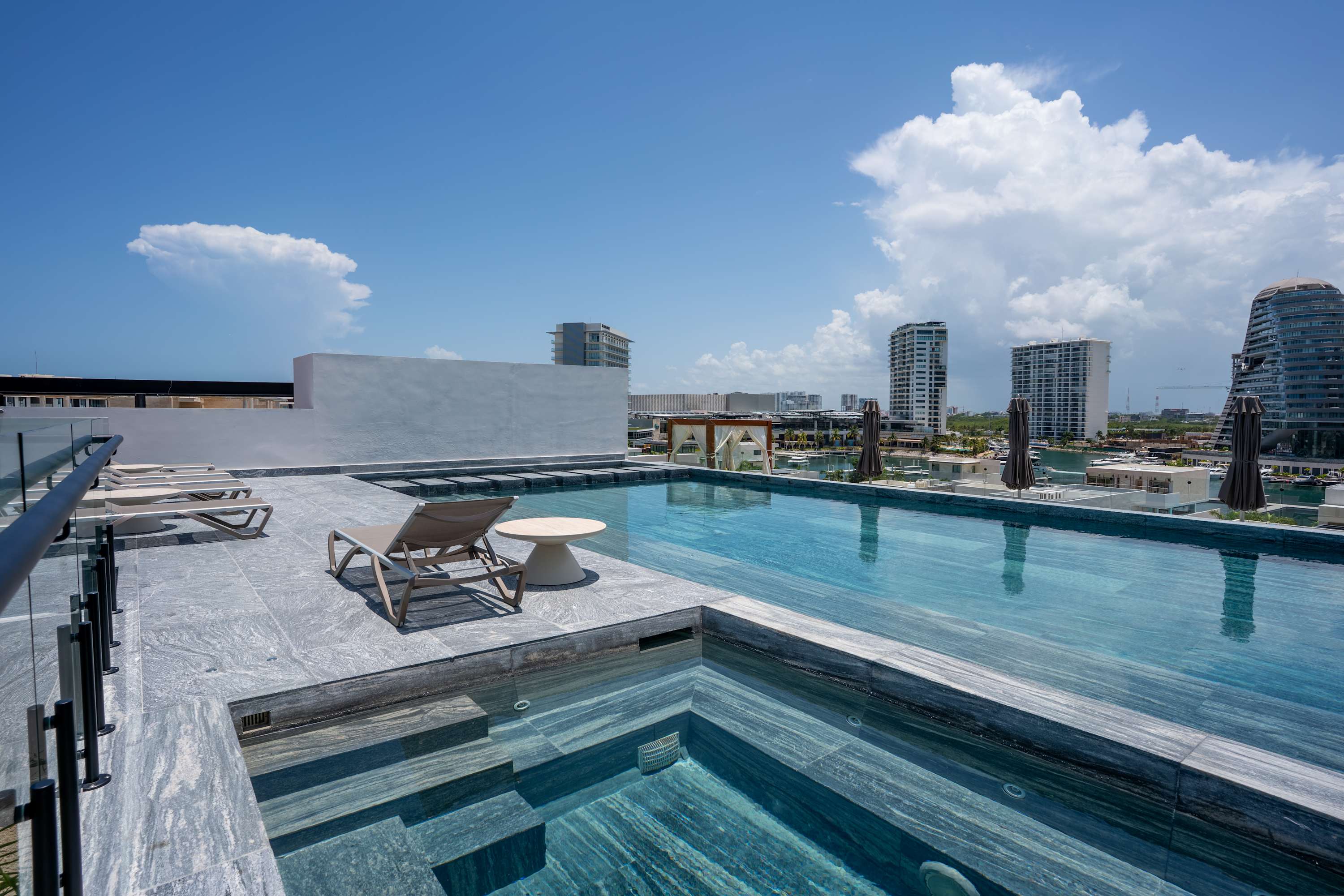 A rooftop infinity pool with lounge chairs overlooking a city skyline.