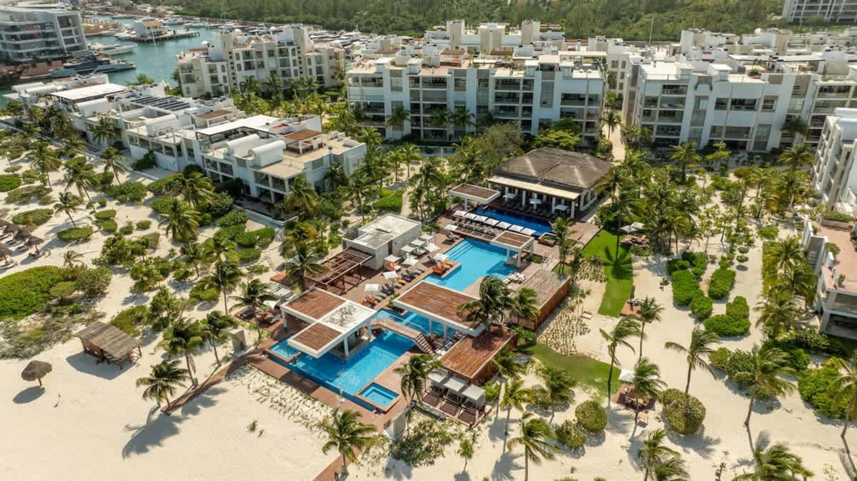 Aerial view of a resort with pools, palm trees, and white buildings on a beach.