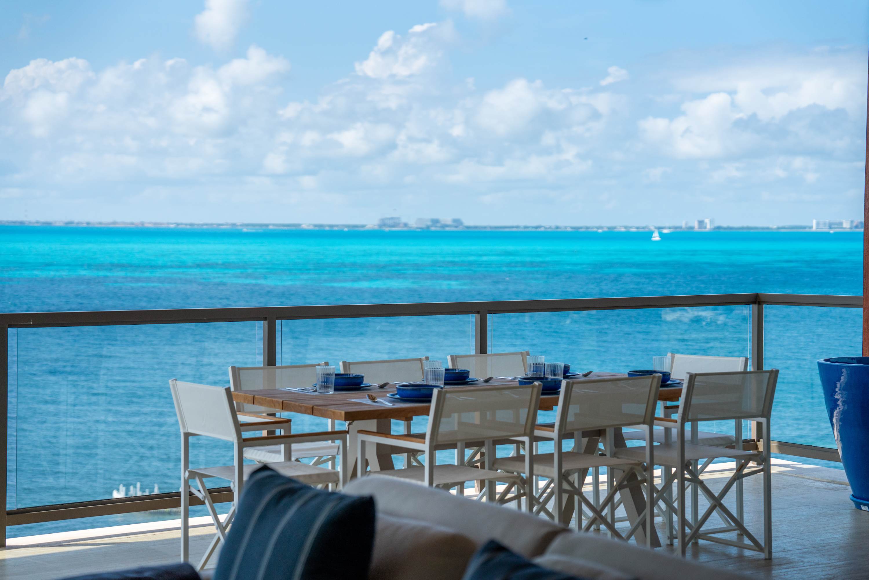 A dining set for eight overlooks a beautiful turquoise ocean under a cloudy blue sky.