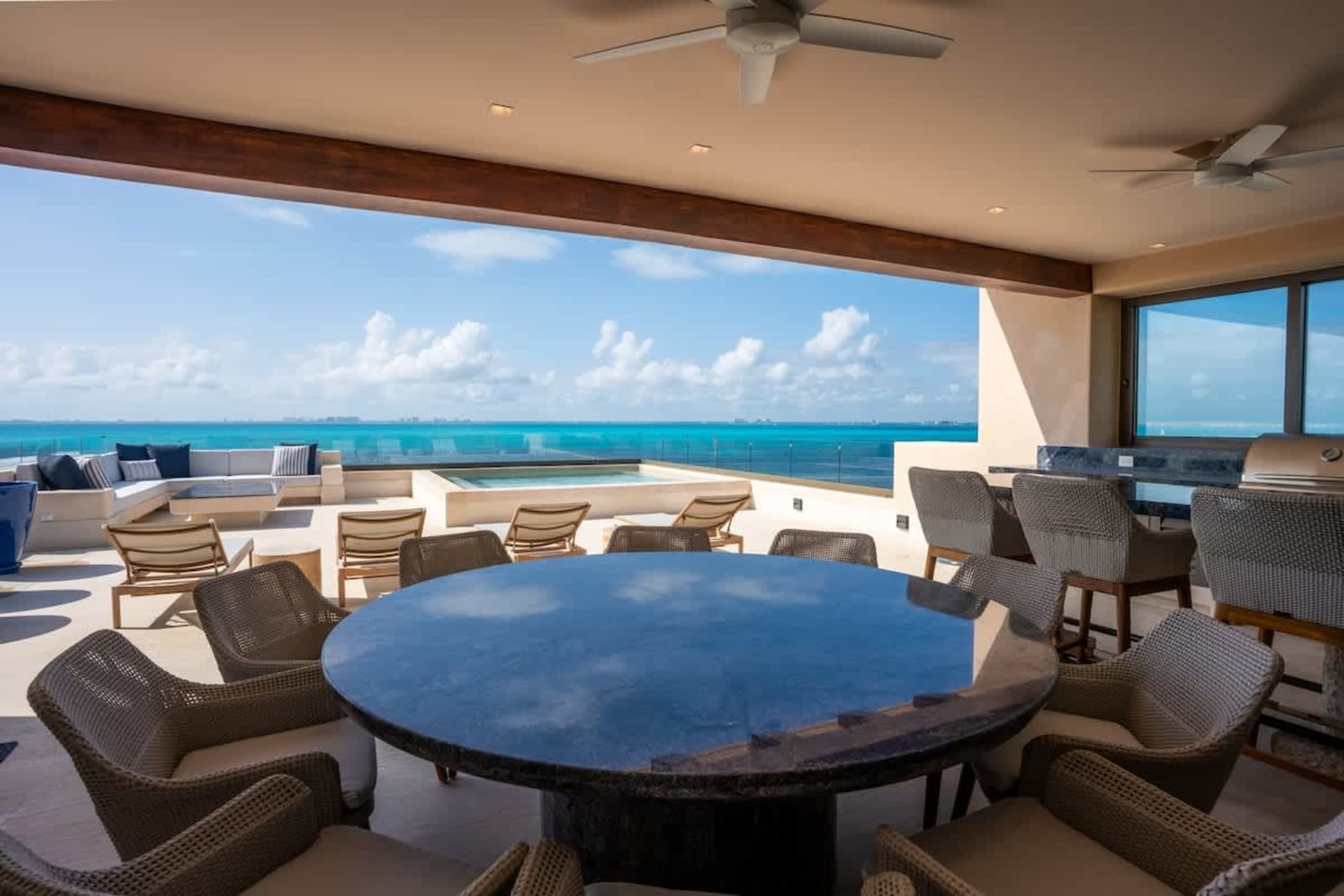 An outdoor patio with a dining table, chairs, lounge chairs, a pool, and a view of the ocean.