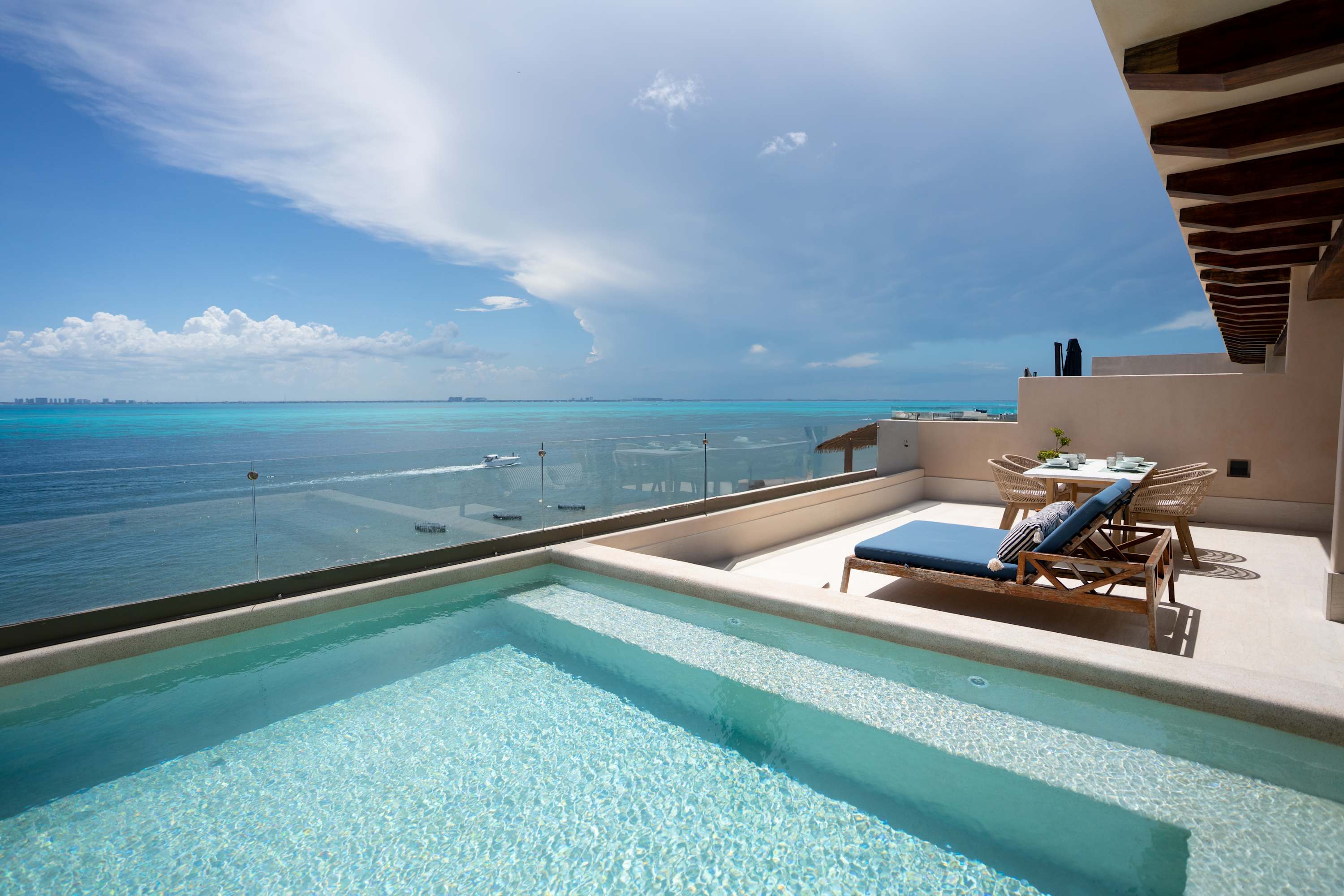 A private pool on a balcony overlooking the turquoise ocean and a distant city skyline.