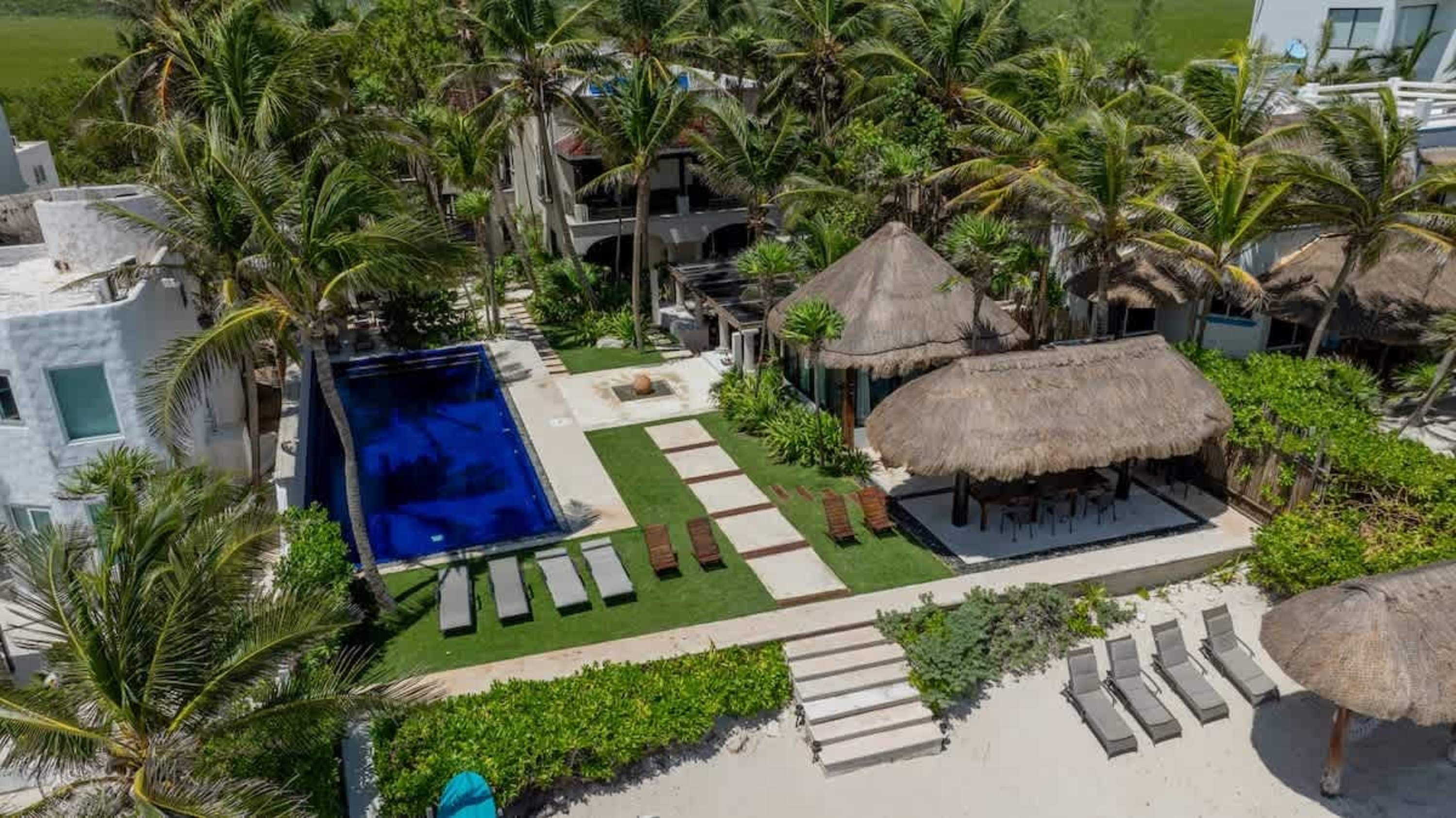 A lush resort with a pool, thatched-roof cabanas, and lounge chairs on a sandy beach.