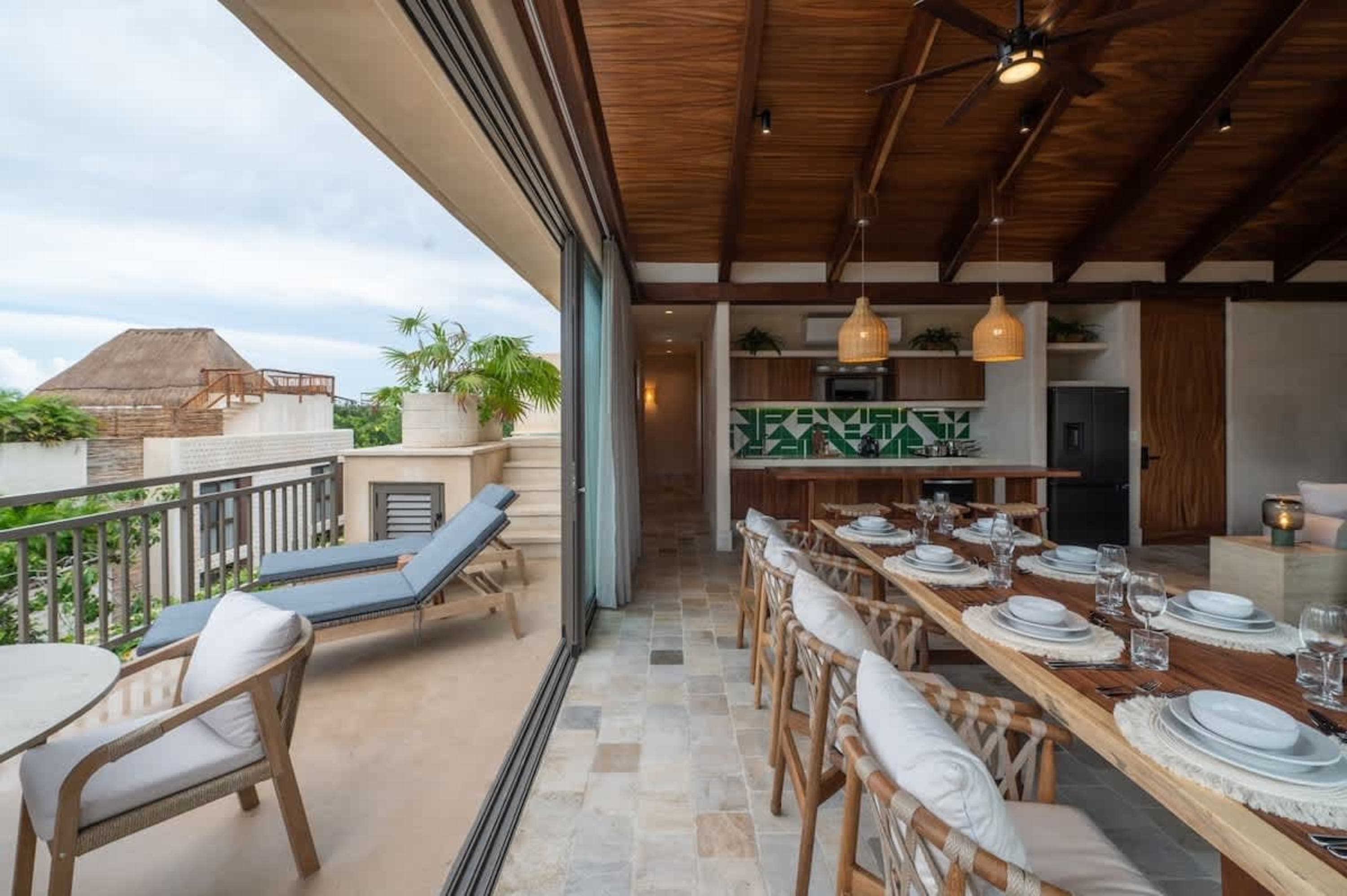 Modern dining area with a long wooden table and chairs, opening to a balcony with lounge chairs.