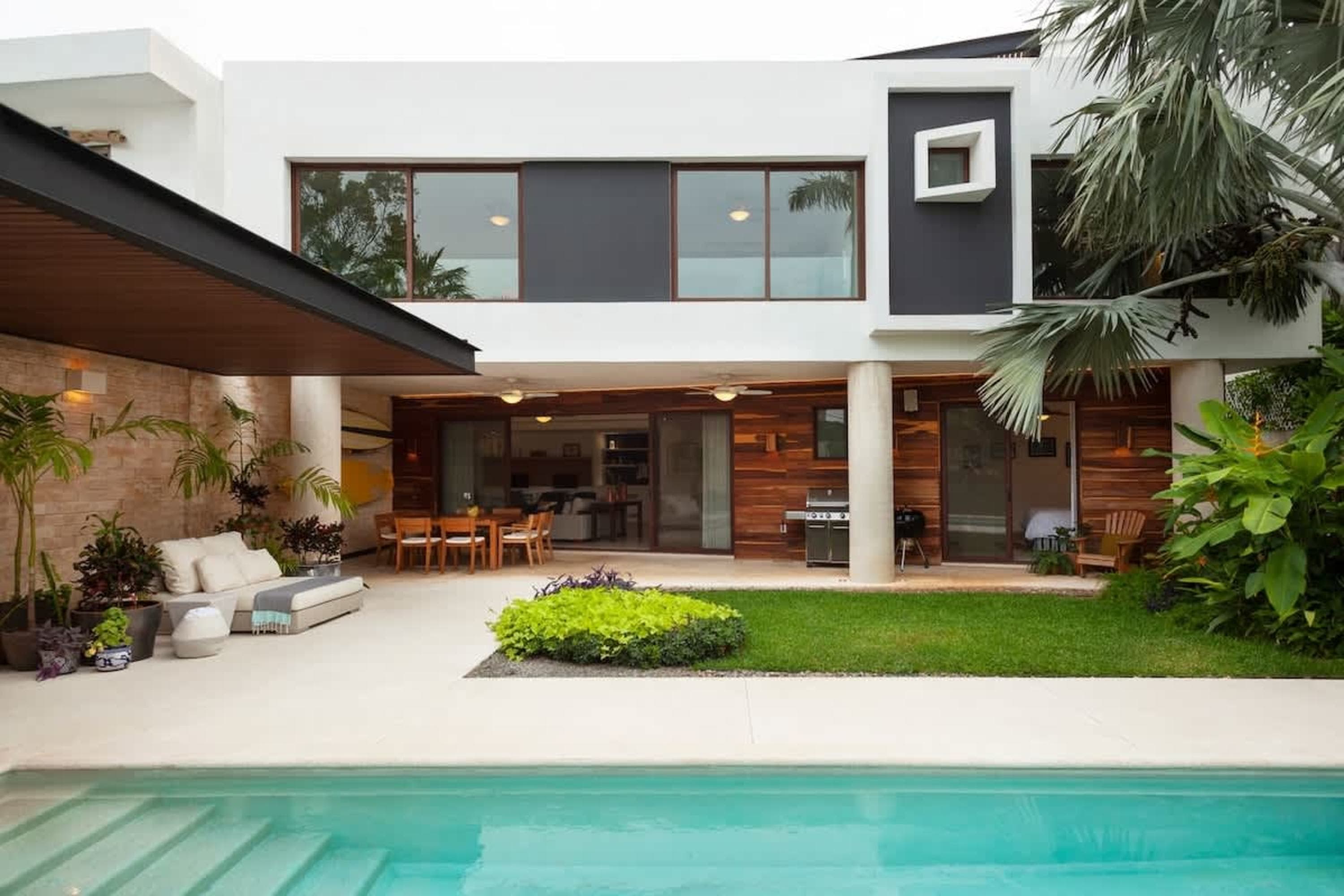 Modern white house with a pool, patio, and lush greenery.