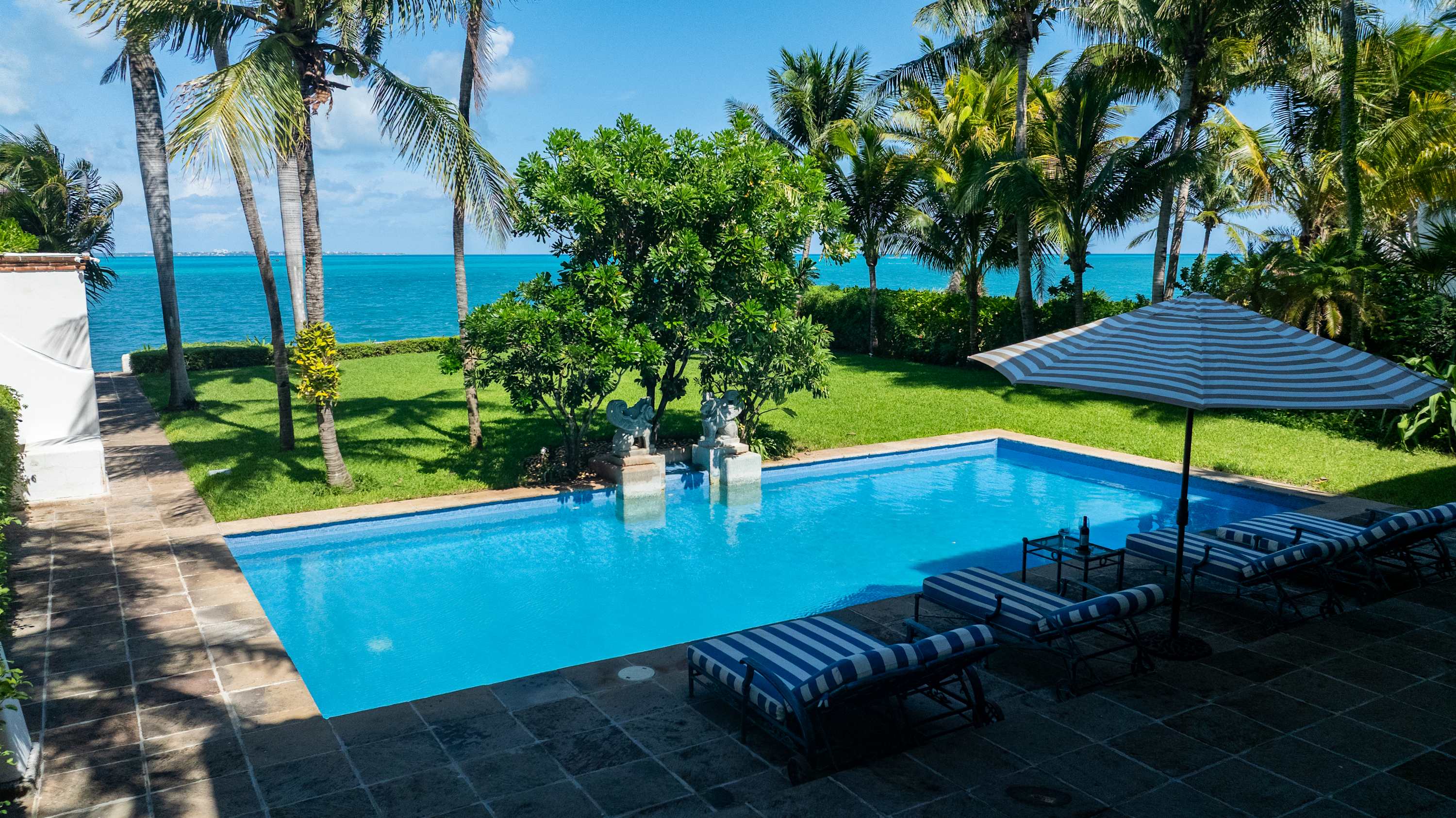 A resort pool and lounge chairs overlook a turquoise ocean.