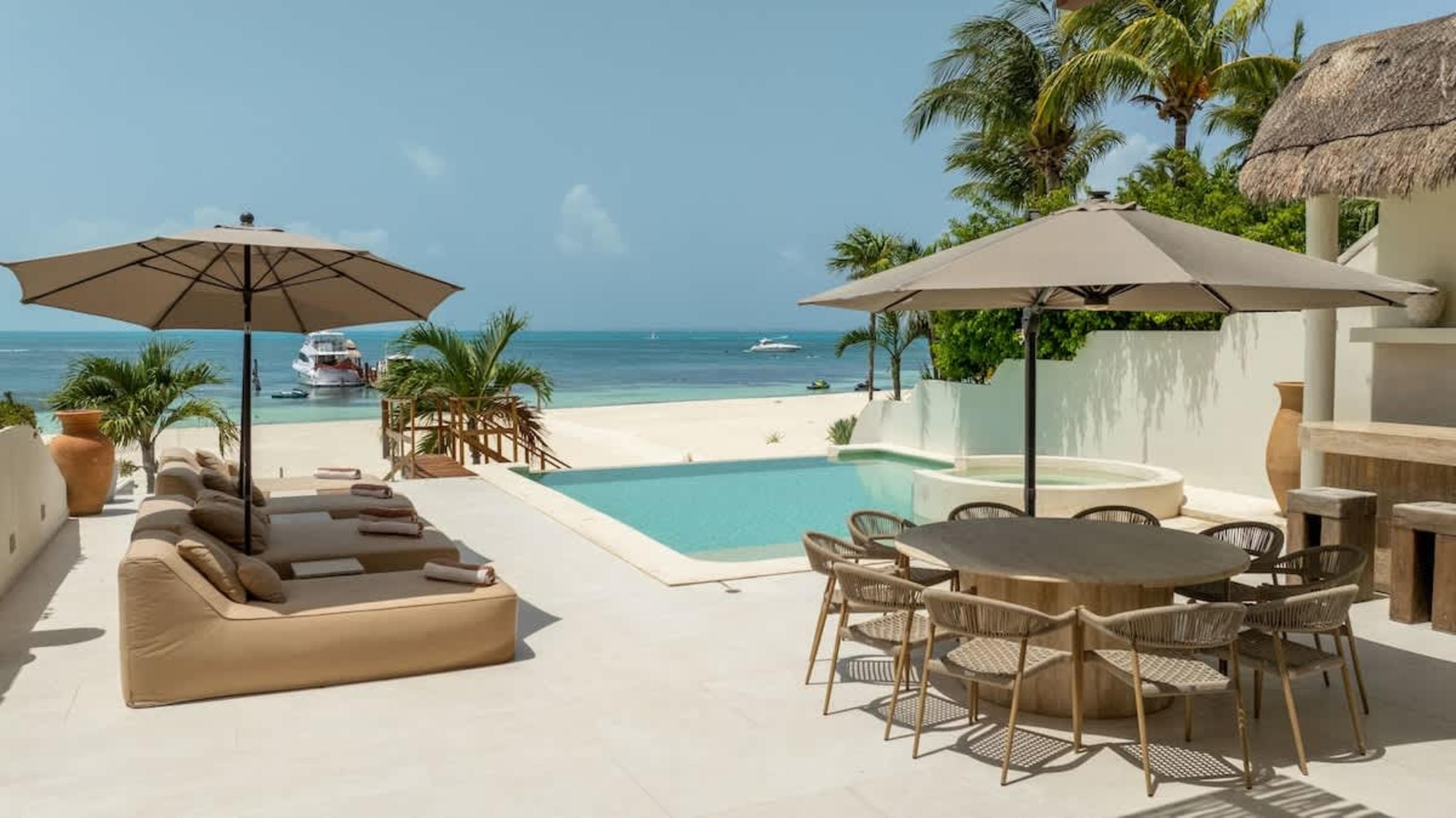 Luxury beachfront patio with lounge chairs, pool, and dining table.